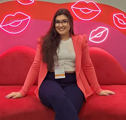 Foto da biomédica doutura Maria Eduarda sentada em uma sofá vermelho
