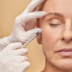 Aplicação de toxina botulínica (botox) em mulher de meia-idade para suavizar rugas e linhas de expressão em uma clínica de estética especializada.